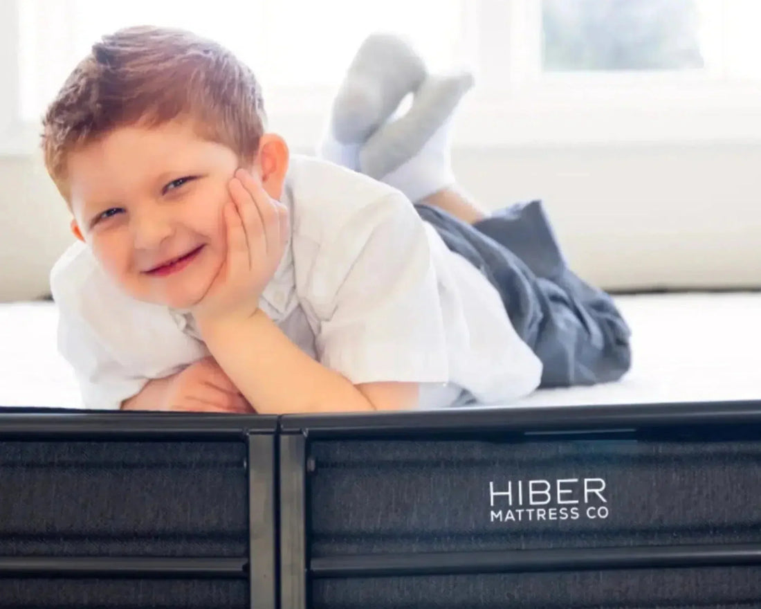 Smiling young boy lying on a Hiber Mattress Co. bed, enjoying comfort and support in a bright bedroom.
