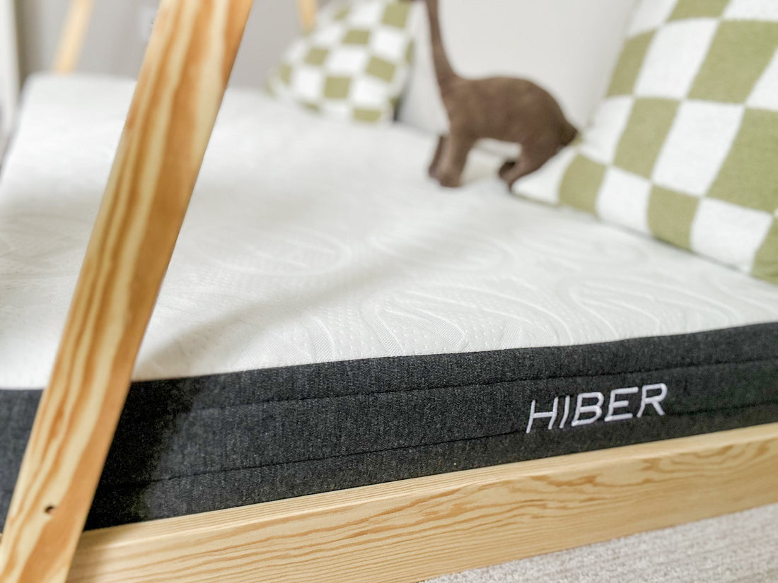 Close-up of a HIBER mattress on a wooden bed frame in a kids' room, featuring a plush top and supportive base—ideal for comparing firmness levels in side, back, or stomach sleeping.