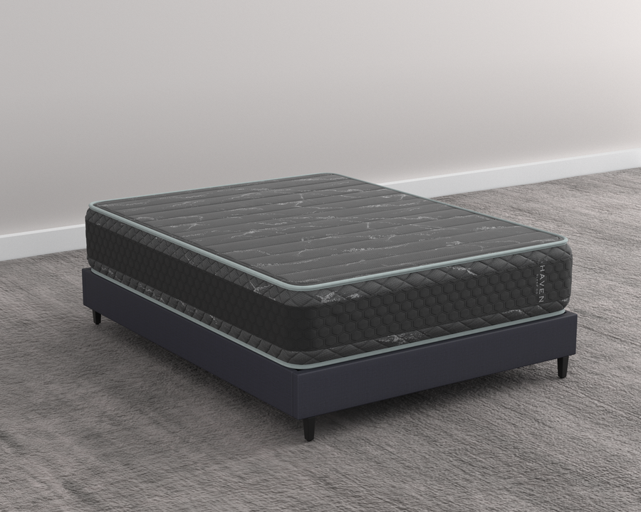 Canada's first reversible HD hybrid mattress by Haven, engineered for plus-size sleepers. The mattress features a sleek black and gray design with 7-zone HD coils and contouring NaturFoam. Ideal for heavy-duty support, offering both very firm and extra firm sides. Shown on a minimalist bed frame, this mattress provides advanced cooling with bamboo cover and copper-infused layers for a clean, cool sleep environment.