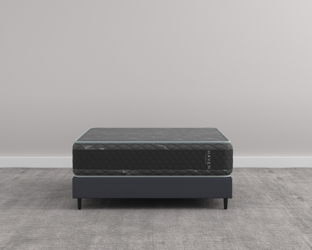 Front-facing view of the Haven HD Hybrid mattress on a minimalist bed frame, highlighting its sleek black and gray design. This heavy-duty mattress, made in Canada, is engineered for plus-size sleepers, featuring 7-zone HD coils and contouring Talalay latex for firm and extra-firm support. The image showcases the mattress’s robust build and elegant finish, ideal for providing superior comfort and durability.