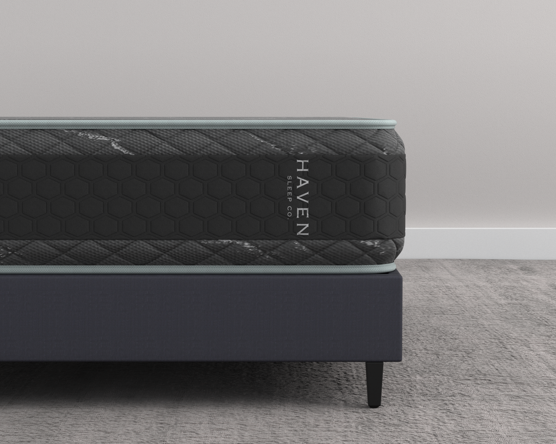 Close-up side view of the Haven HD Hybrid mattress, displaying its black and gray honeycomb pattern design. The mattress is tailored for plus-size sleepers, featuring 7-zone HD coils and Talalay latex for firm and extra-firm support. The Haven Sleep Co. branding is visible, emphasizing the mattress's durable construction and premium quality, designed for enhanced comfort and long-lasting use.