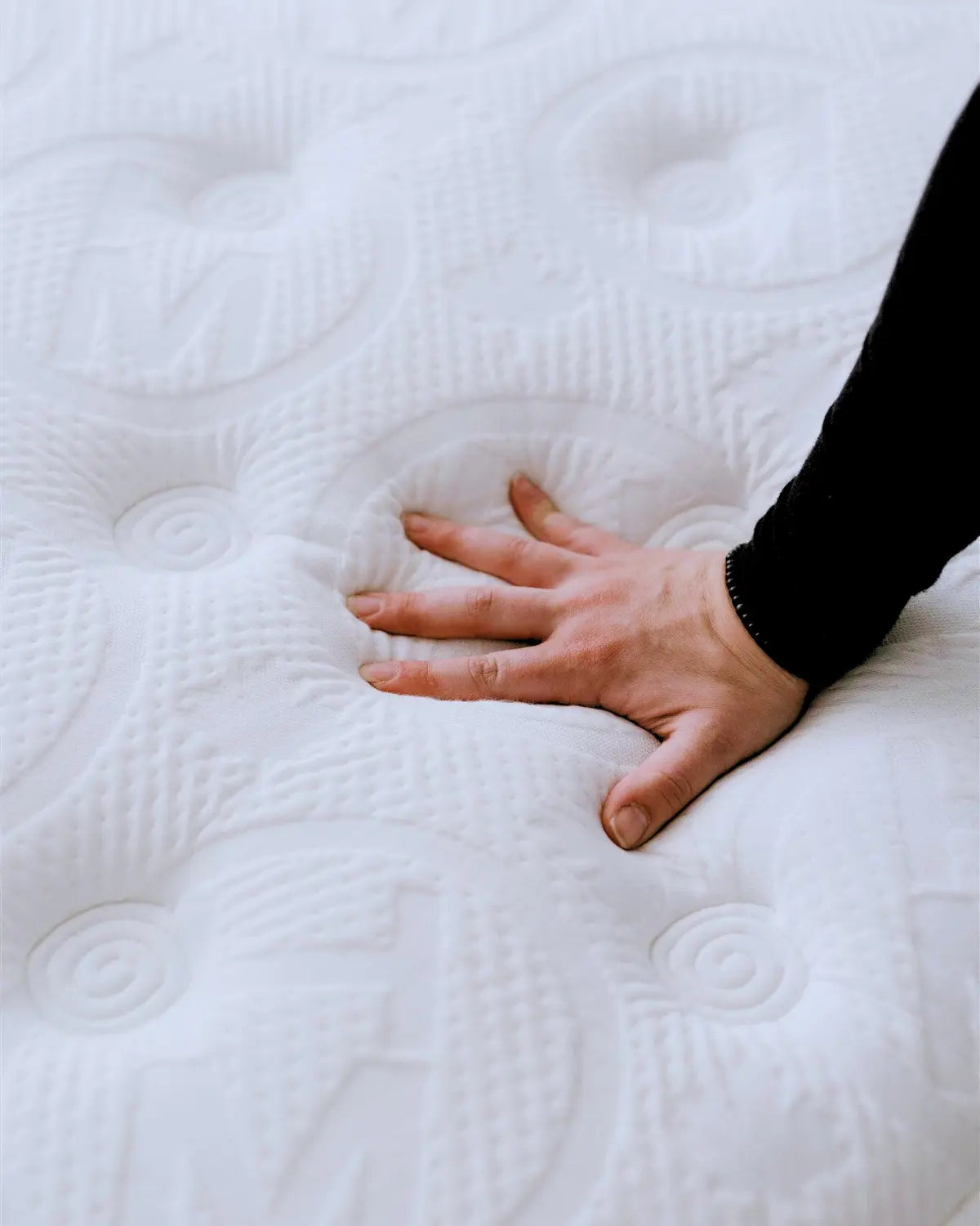Hand pressing into a white mattress to demonstrate firmness