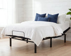 Bed with white bedding and blue pillows in a room with wooden flooring and white walls.