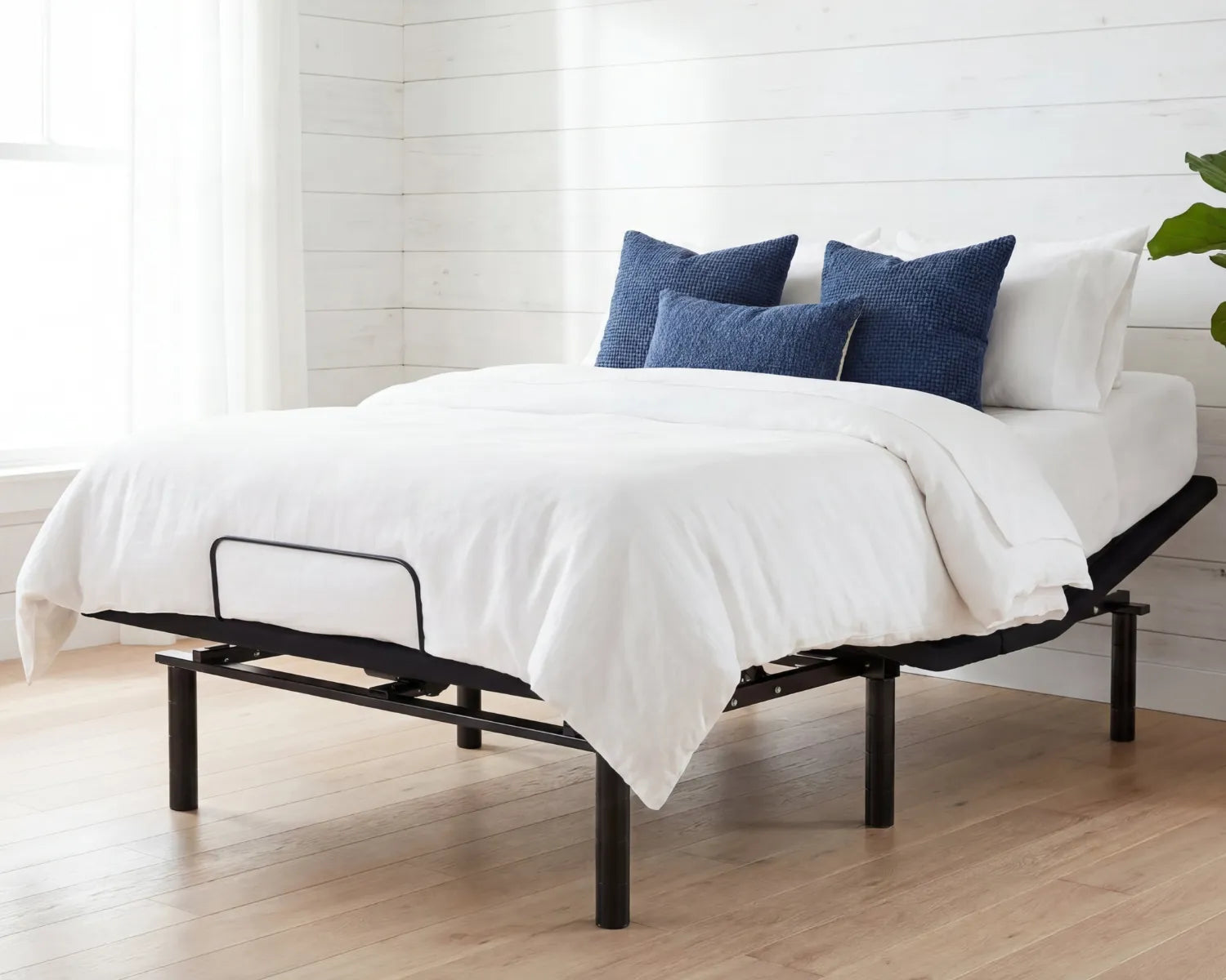 Bed with white bedding and blue pillows in a room with wooden flooring and white walls.