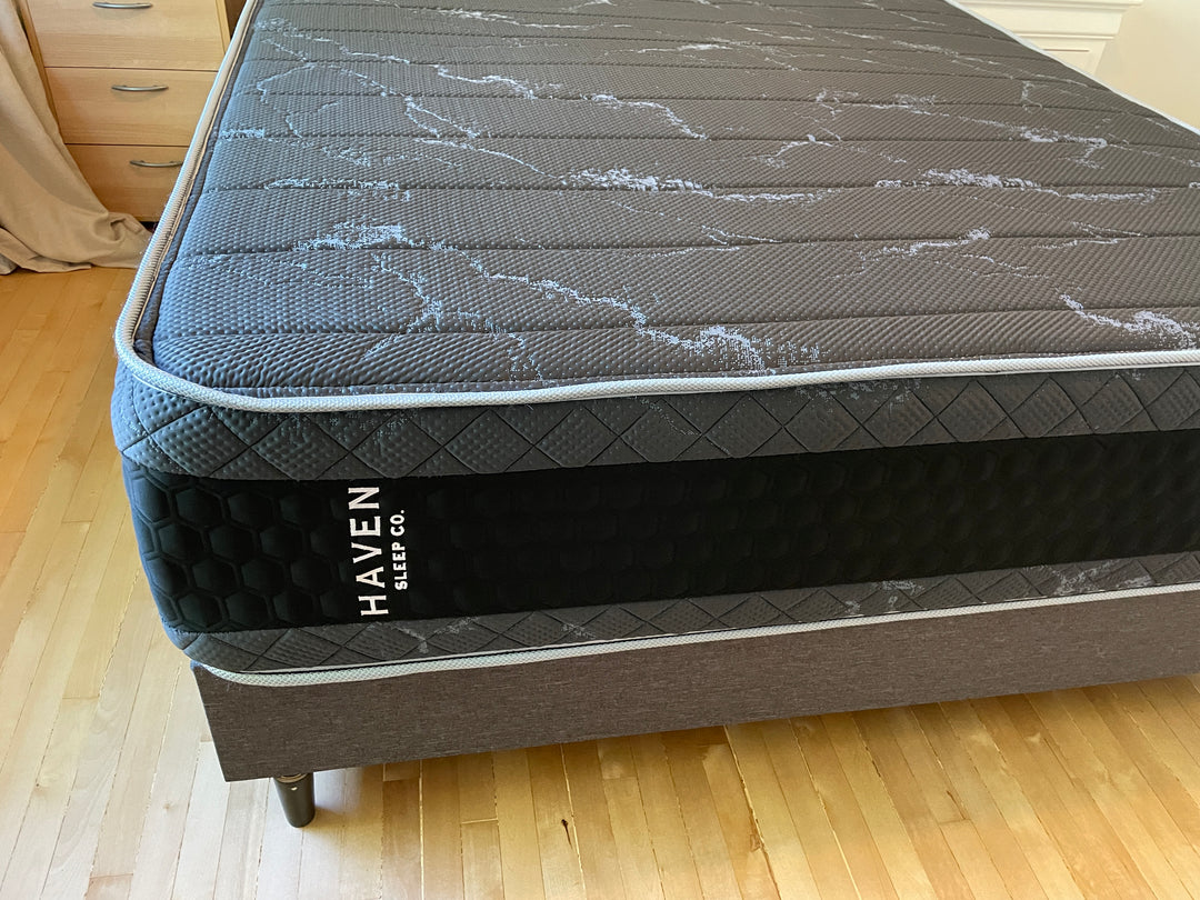 Top corner view of the Haven HD Hybrid mattress, showcasing the black and gray textured surface with the Haven Sleep Co. branding visible on the side. Designed for plus-size sleepers, the mattress features 7-zone HD coils and Talalay latex for enhanced firm and extra-firm support. The image highlights the premium craftsmanship and durable materials, ideal for providing a supportive and comfortable sleep experience.