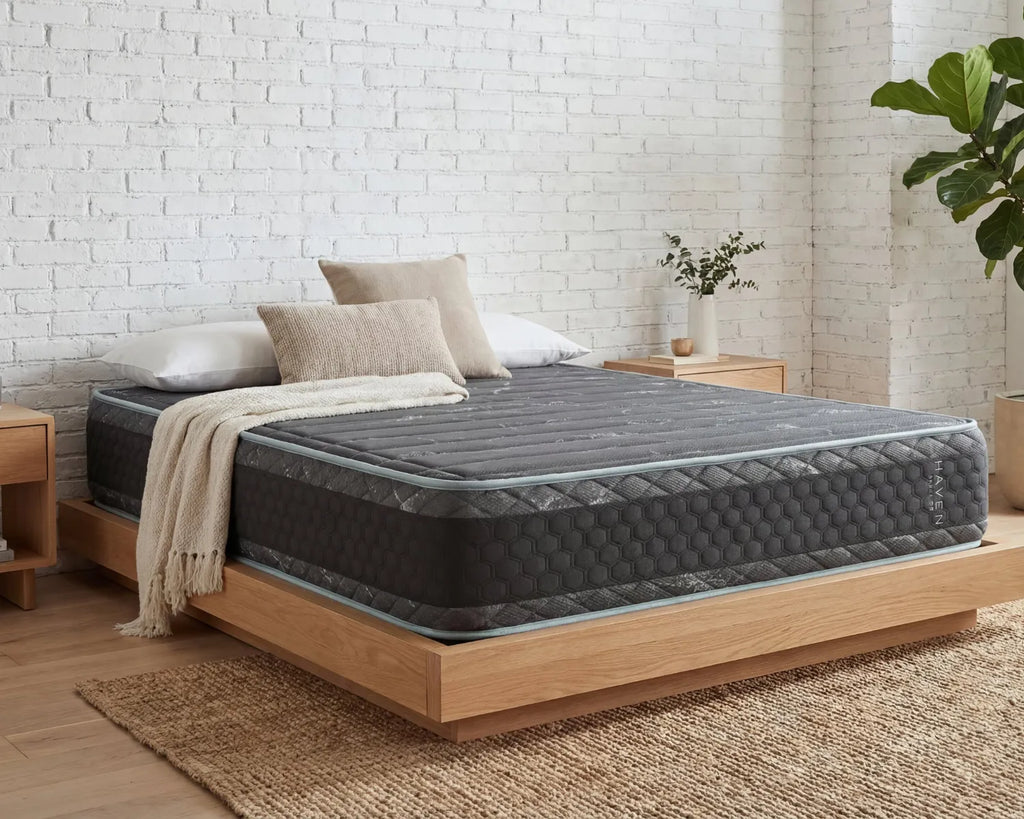 Gray mattress on a wooden bed frame against a white brick wall.