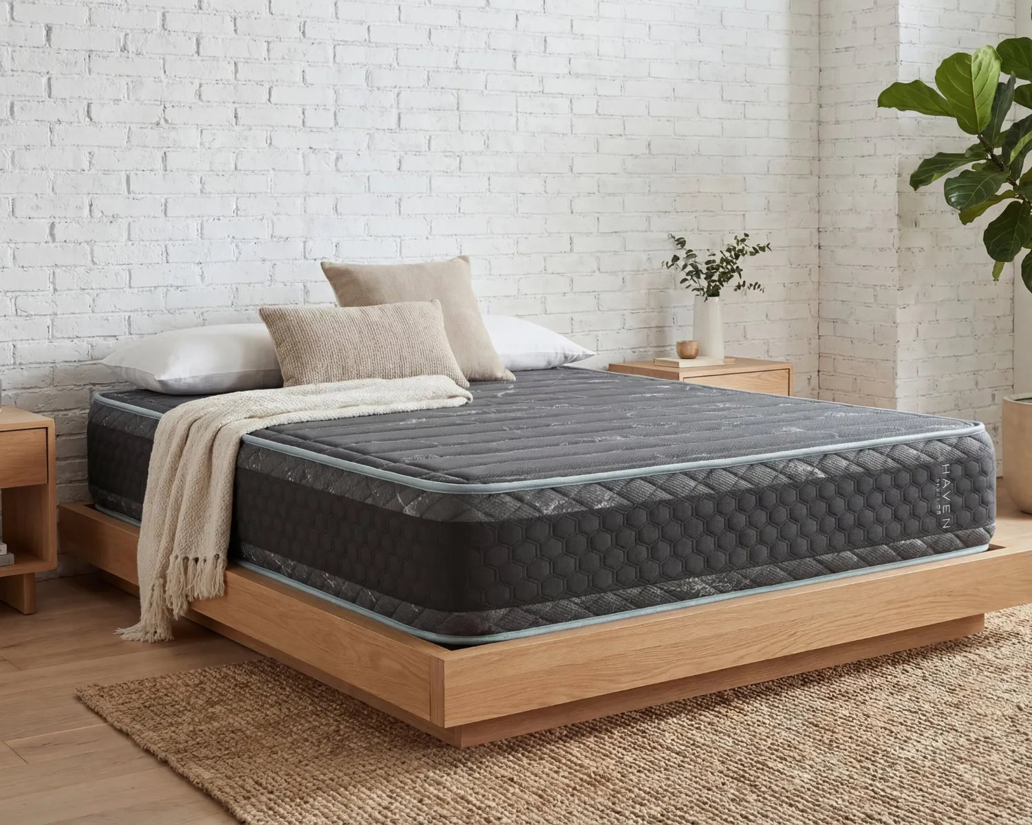 Gray mattress on a wooden bed frame against a white brick wall.