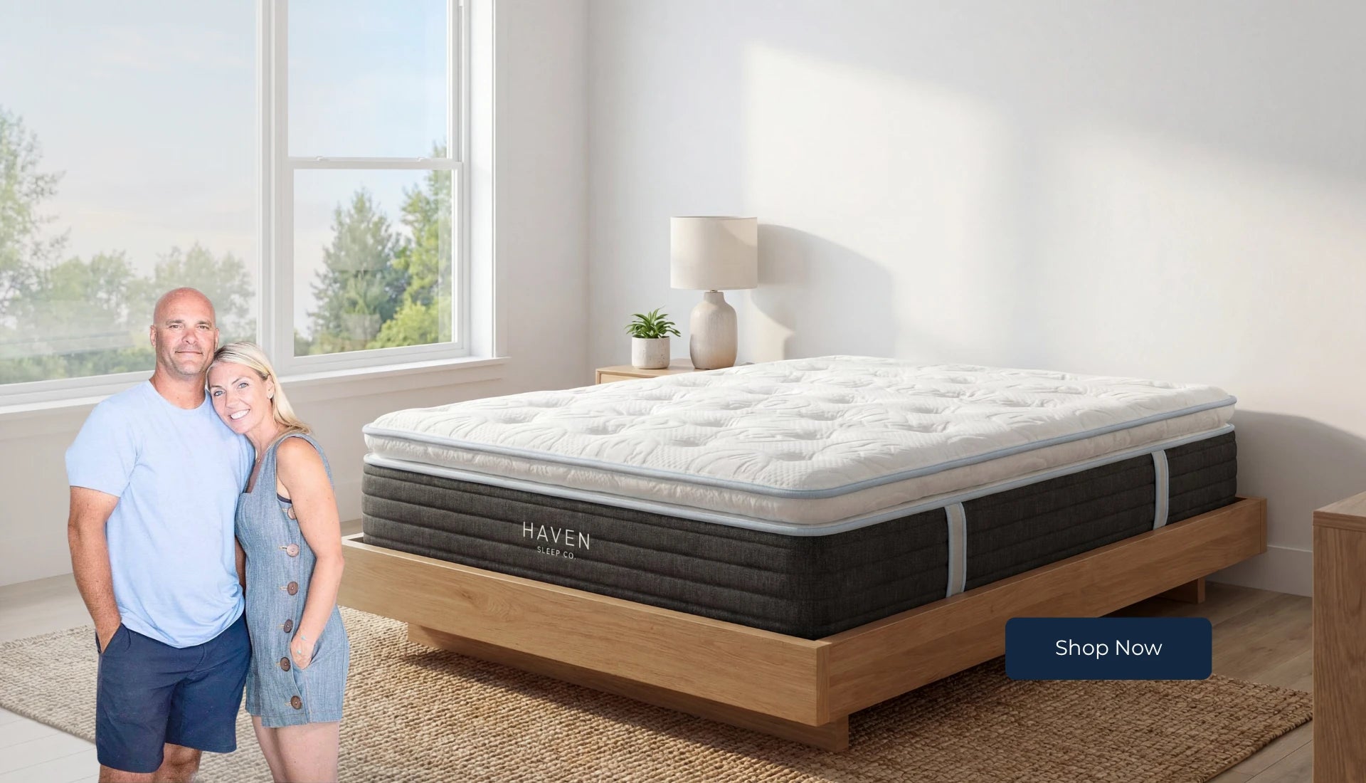 Man and woman standing next to a Haven mattress in a room with large windows.