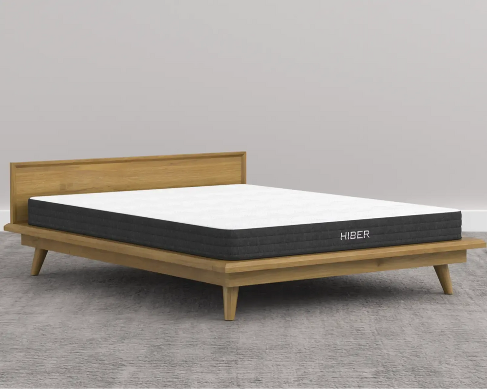 Mattress on a wooden bed frame with 'Hiber' branding against a gray background