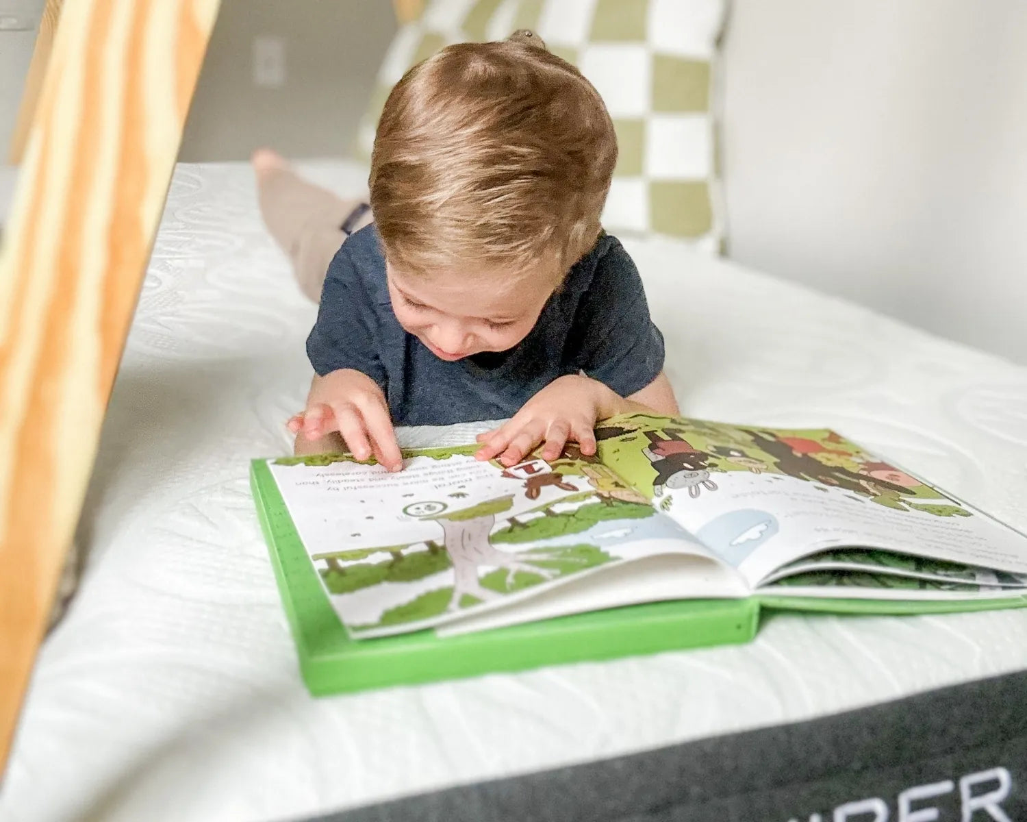 Child reading a book on a mattress with a wooden crib frame in the background