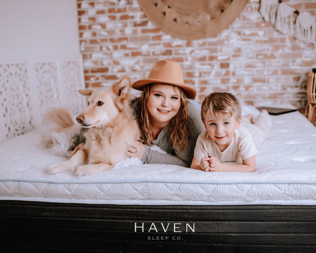Two children and a dog lying on a Haven Sleep Co mattress with a brick wall background.