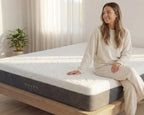 Woman sitting on a Haven mattress in a bright room with curtains and a plant.