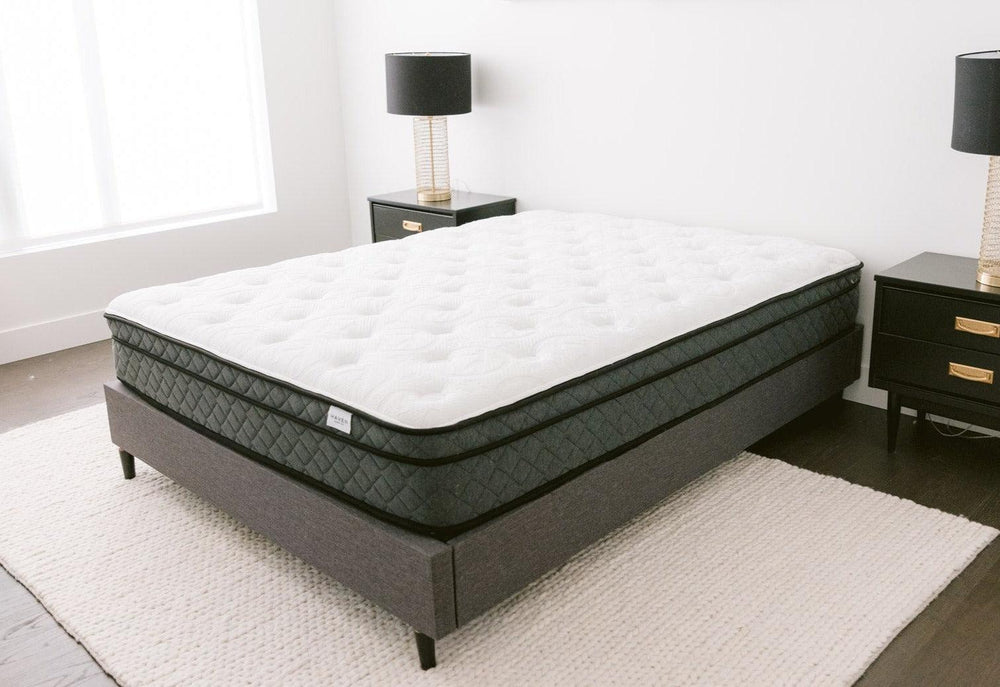 Image of a Haven Pocket Coil Mattress with a white quilted top and dark grey sides, displayed in a modern bedroom setting with a grey upholstered bed frame, black nightstands, and a light-colored area rug. The mattress features 884 individually wrapped coils, a bamboo cover with cool touch technology, and plant-based foams for enhanced sleep comfort and support. Made in Canada.