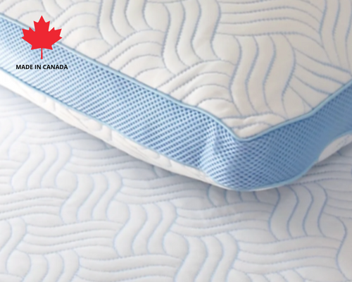Close-up of a Canadian-made cooling memory foam pillow with blue mesh sides and wavy stitch pattern, shown on matching mattress surface, Made in Canada label in top left corner