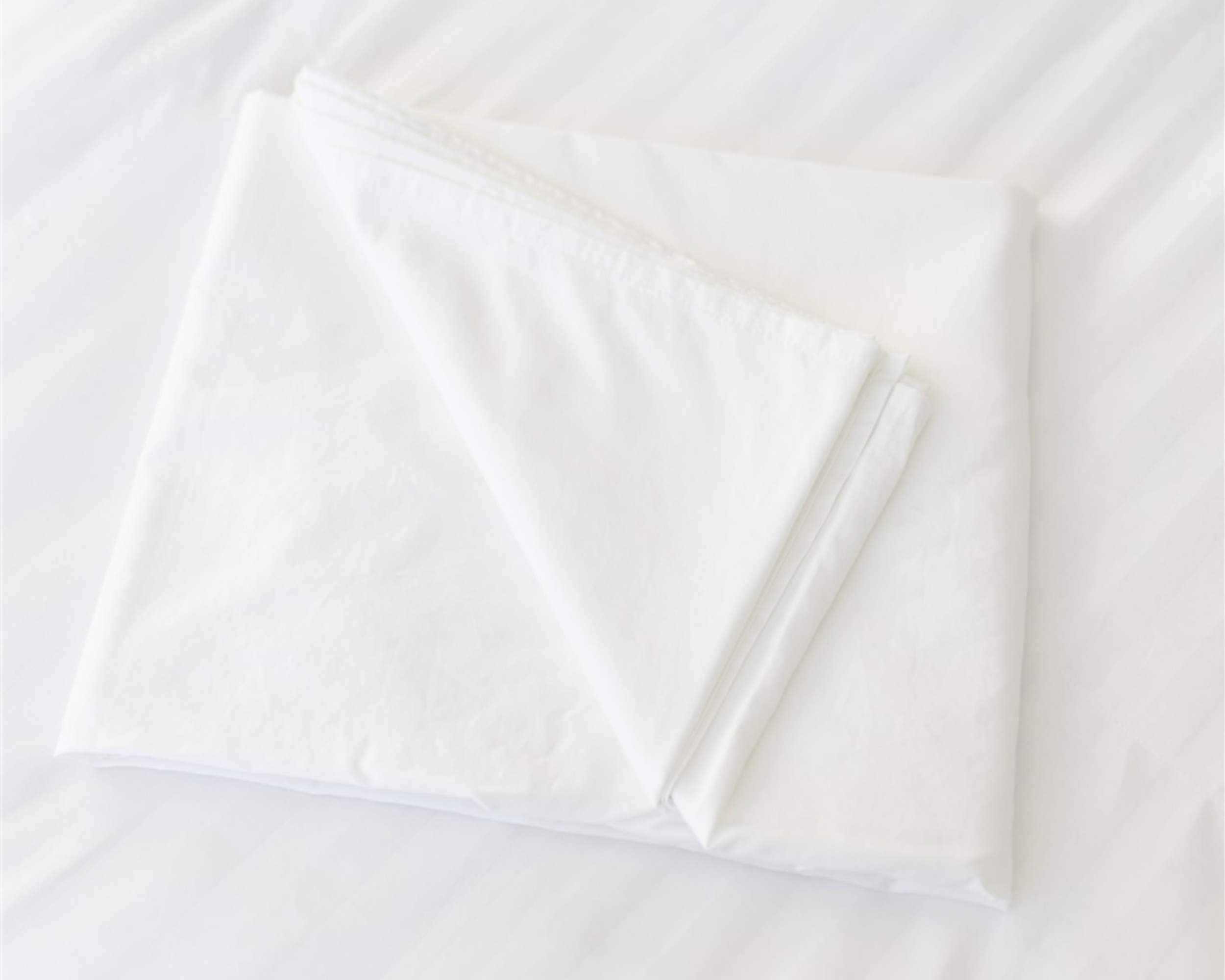 White organic cotton sheets folded neatly on a bed, showcasing their soft, stonewashed finish. These eco-friendly Bedface linens are made from 100% organic cotton and are certified by Oeko-Tex® and GOTS, ensuring safe and sustainable production.