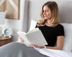 blonde women sitting up reading a book in her bedface sheets set