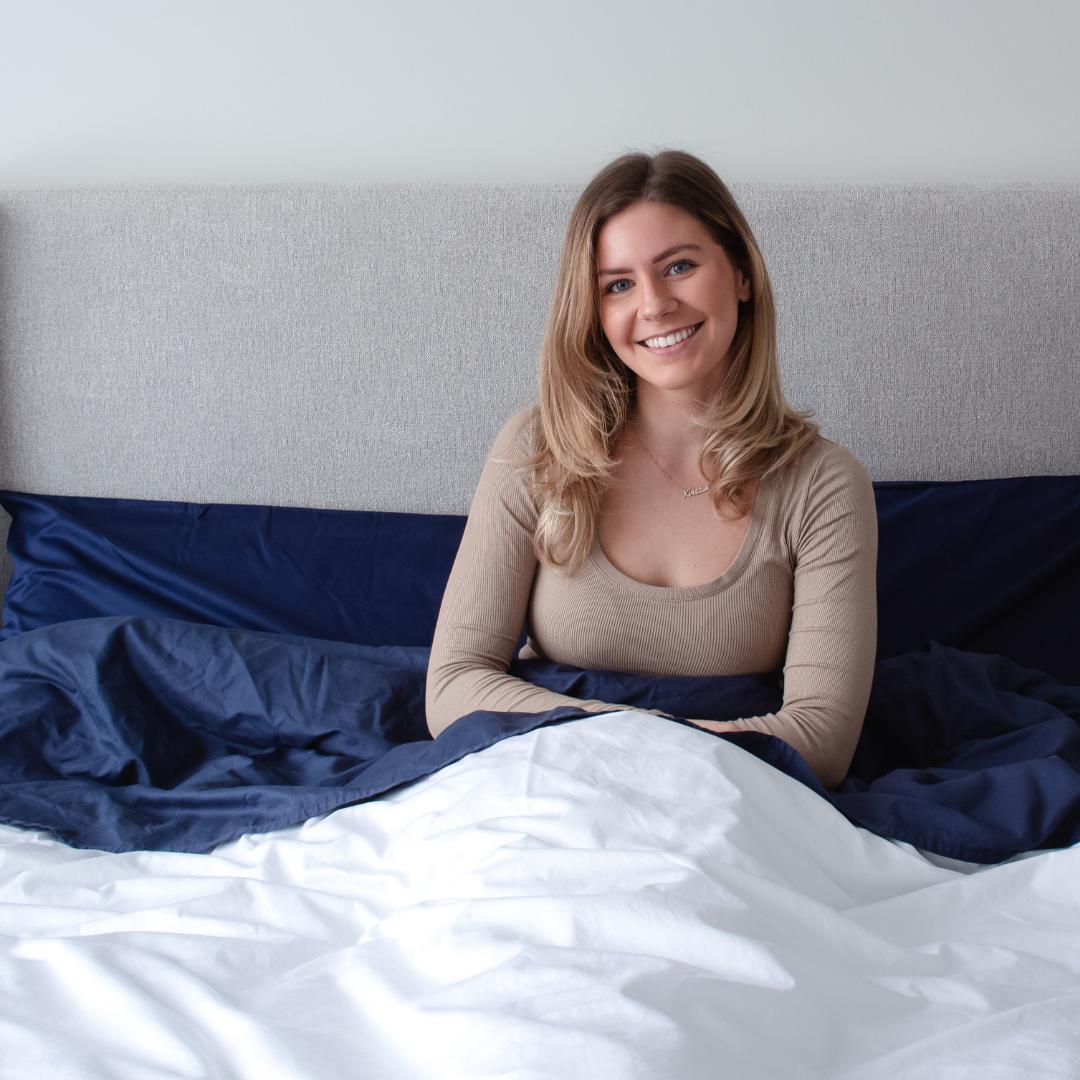 Femme assise dans son lit, souriante, dans un ensemble de draps et une housse de couette Bedface premium - Blanc etoilé et Marine de nuit