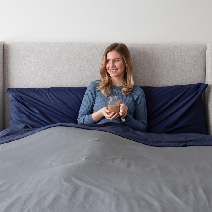 Femme assise dans son lit, souriante, dans un ensemble de draps et une housse de couette Bedface premium - Gris tempête et Marine de nuit