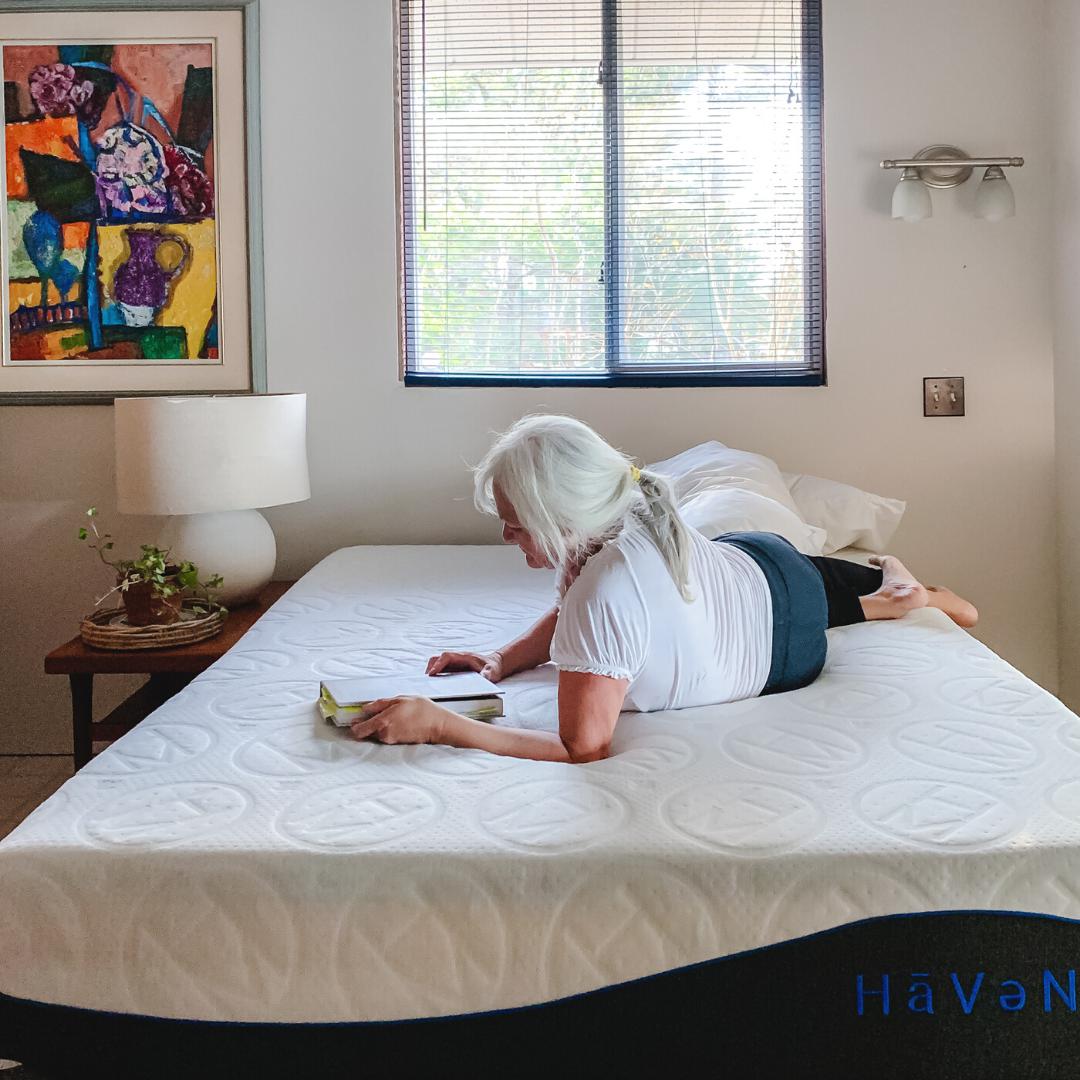Femme âgée portant un T-shirt blanc et un pantalon de yoga, allongée sur un matelas Essential Haven 10" avec un livre à couverture rigide.