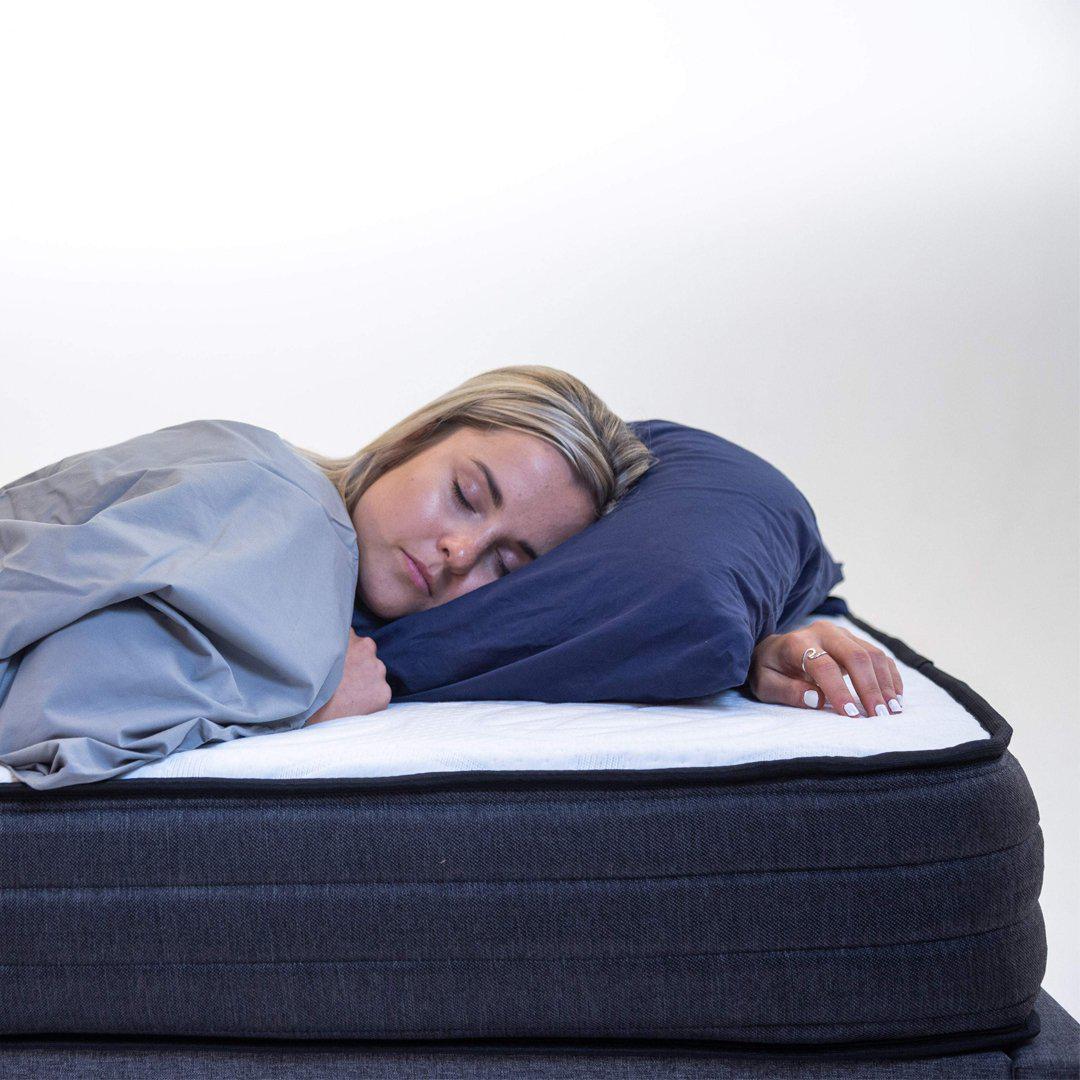 sleeping woman tucked into Bahama Blue top sheet, with nighttime navy pillow and case on top of a 8" Haven recharge mattress